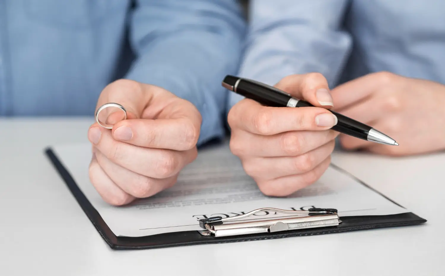 Pareja firmando documento de capitulaciones matrimoniales con el hombre aguantando un anillo y la mujer con el boligrafo