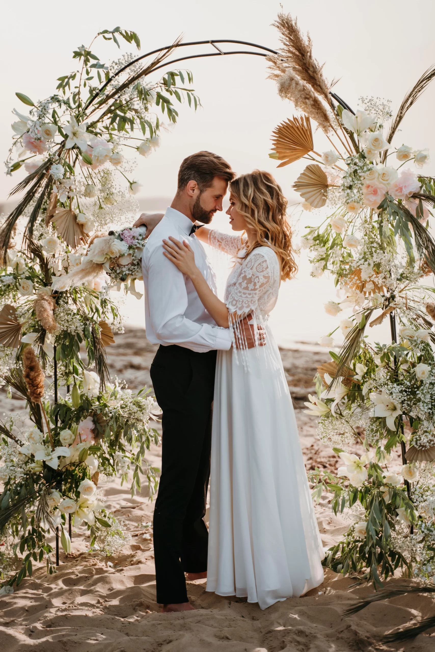 Hombre y mujer recién casados en la playa con un arco lleno de flores